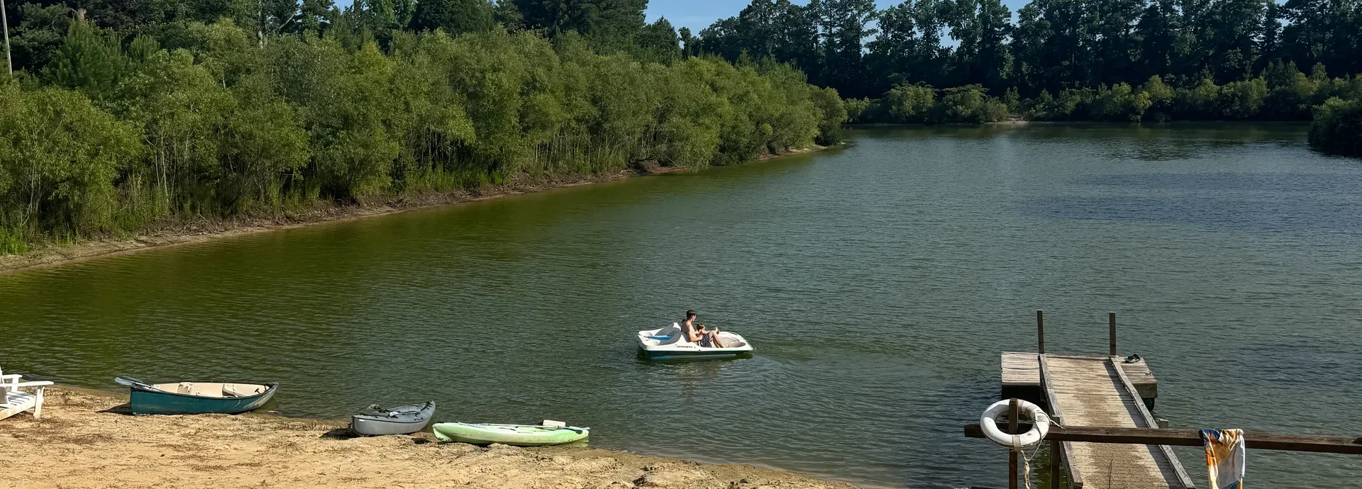 Sandy swim beach on Lake Georgia with kayaks, a paddle boat, and the dock